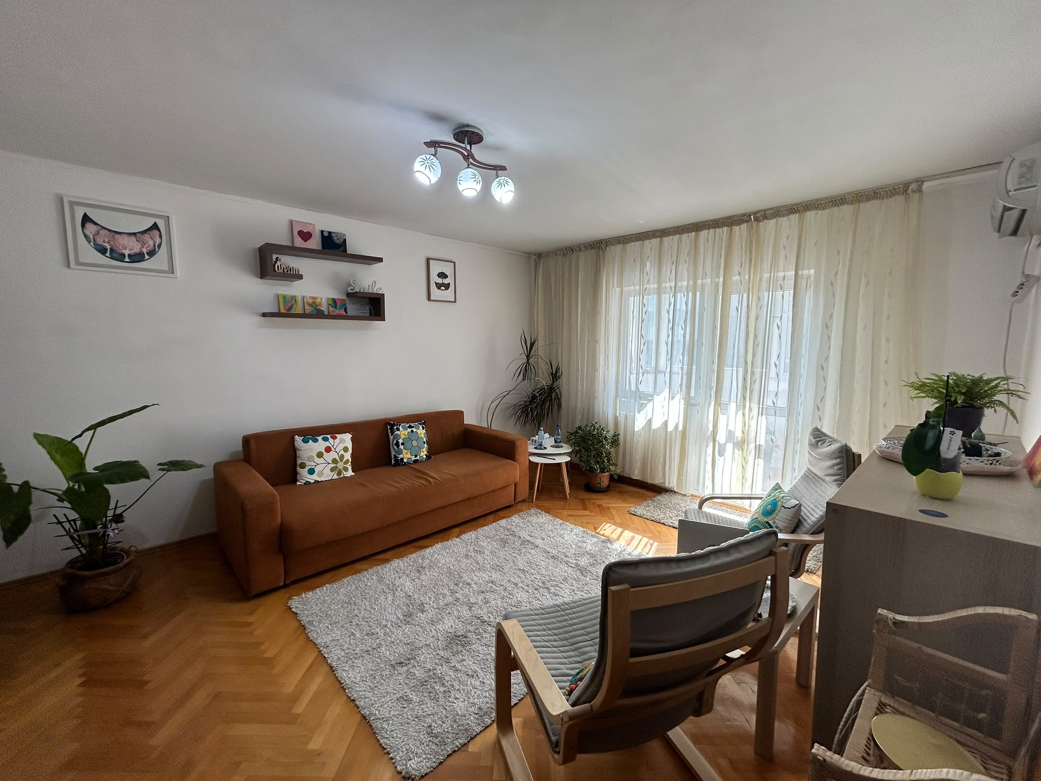 Cabinetul văzut în ansamblu, cu canapea, fotolii de lemn deschis, plante și perdele translucide